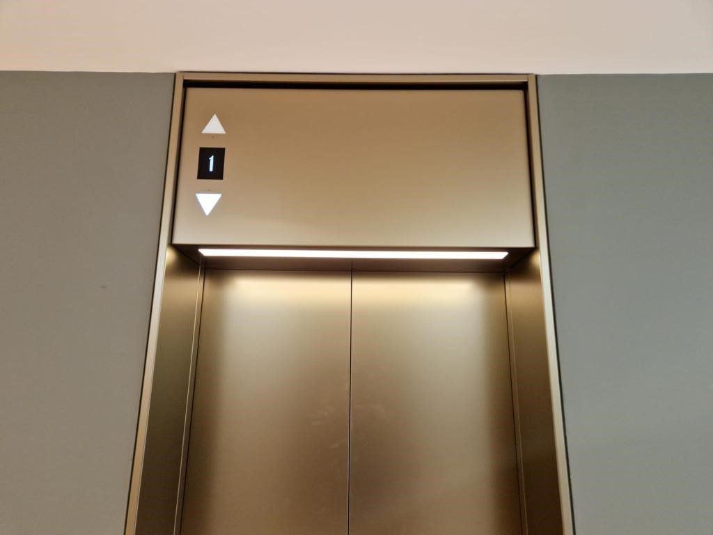 A metallic elevator with two doors and one lift button.