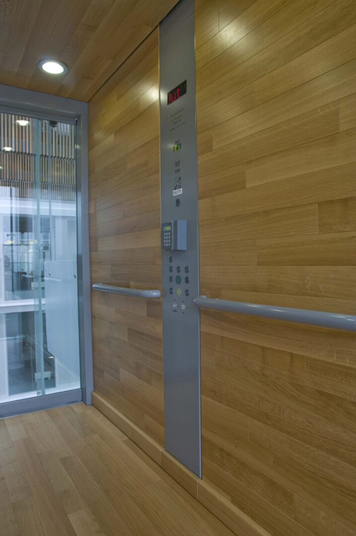 A wooden wall with a metal door and glass elevator.