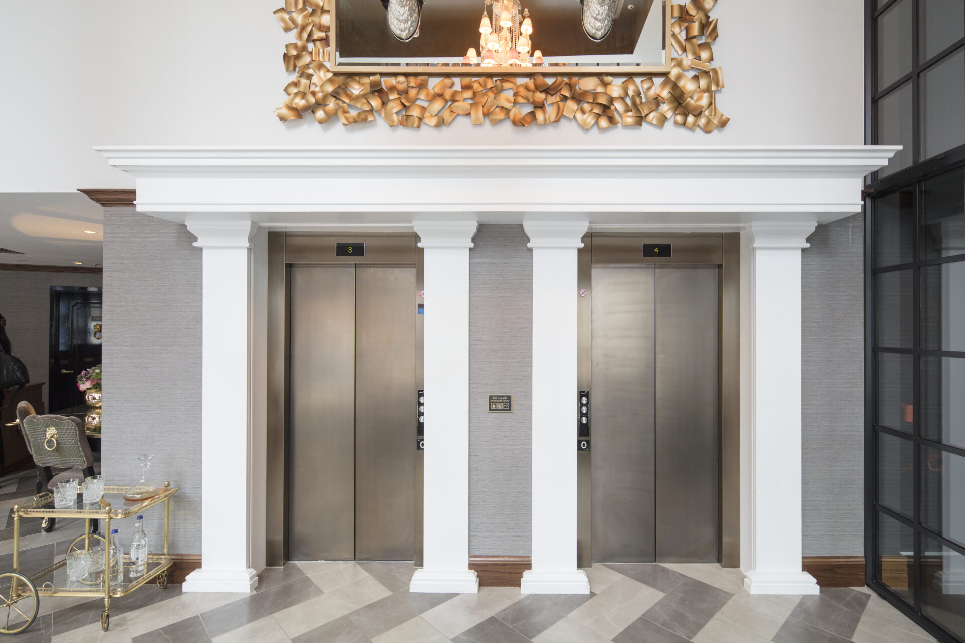 Two elevators in a room with pillars and a mirror.